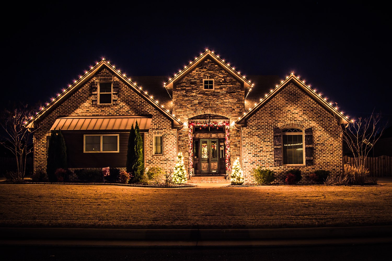 Brick and stone home with warm C9 roofline lights and lit entry